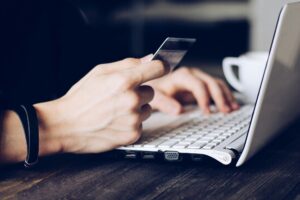 Eine Person tippt auf einem Laptop und hält gleichzeitig eine Kreditkarte, bereit für eine Online-Transaktion, symbolisch für E-Commerce.